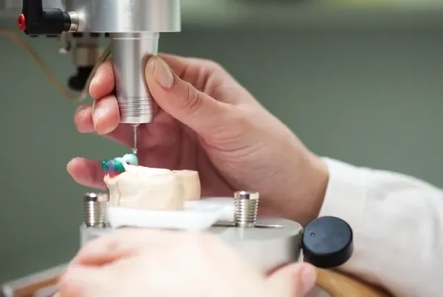 A person is using a machine for medical manufacturing to make a tooth.